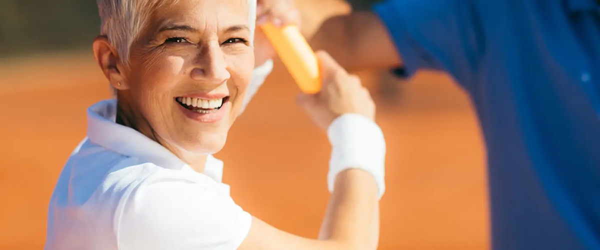 Smiling woman playing tennis, promoting active spine and joint health with Desert Spine and Sports Physicians, Arizona.