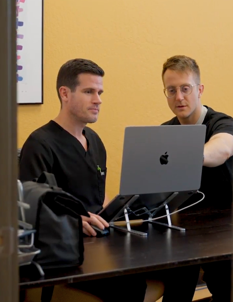 Two Desert Spine and Sports professionals collaboratively review patient data on a laptop, enhancing medical treatment accuracy and care.