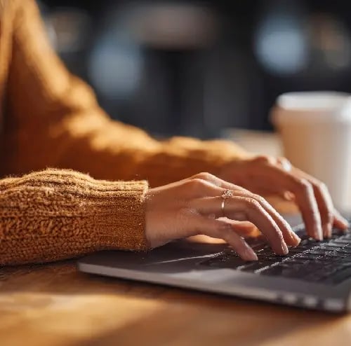 Person typing on a laptop, highlighting digital health solutions. Coffee cup nearby suggests a comfortable, modern workplace.