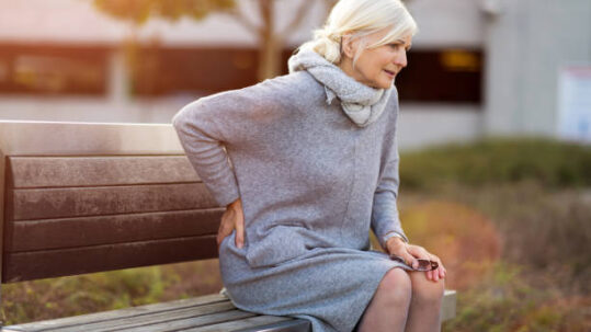 Old lady on a park bench holding lower back in pain