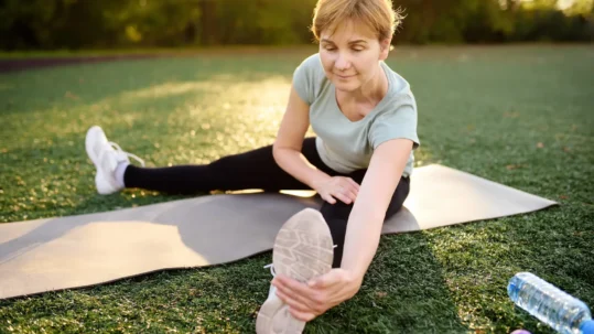 Woman stretching on exercise mat outdoors, promoting joint flexibility and overall wellness.