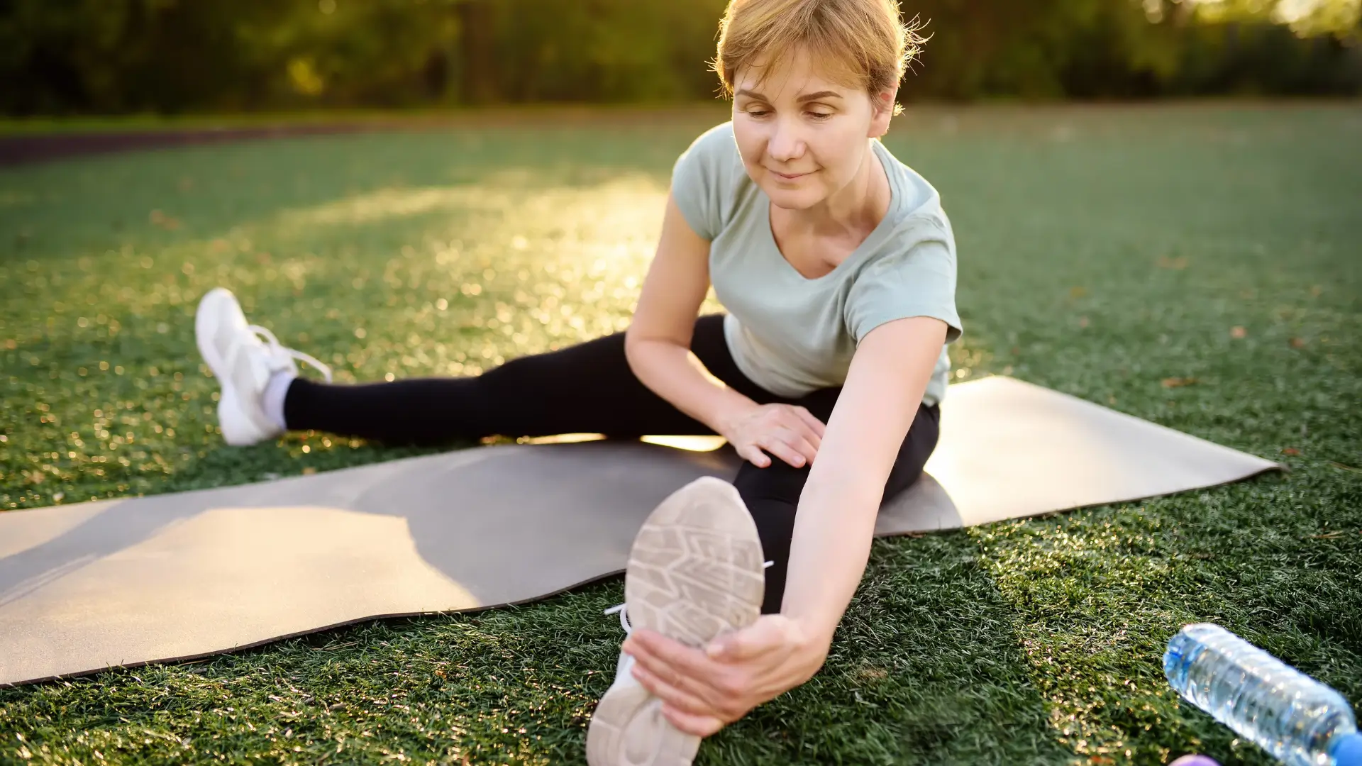 Woman stretching on exercise mat outdoors, promoting joint flexibility and overall wellness.