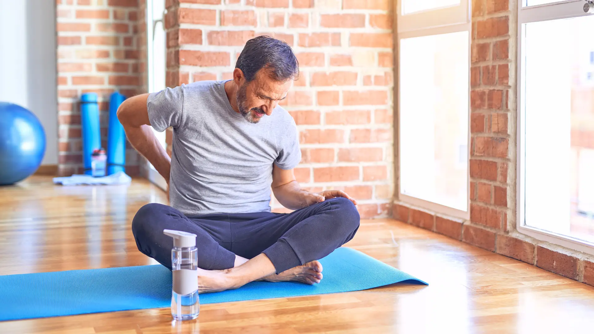 Man experiencing back pain while stretching on a yoga mat.